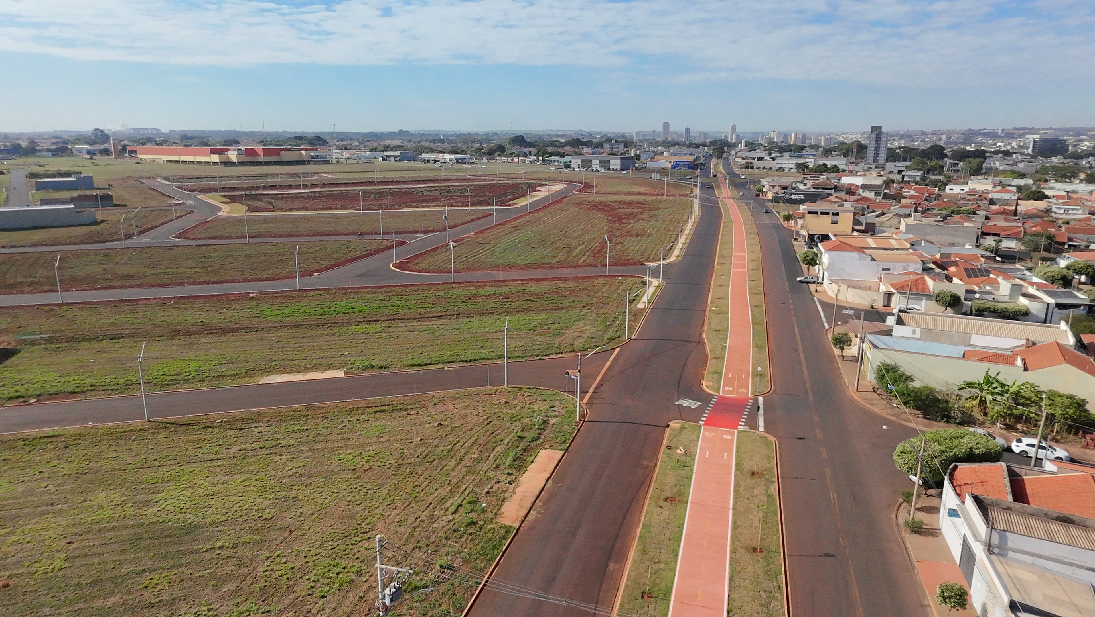 Vista aérea do Bella Verona Boulevard em Maio de 2026, com avenida pavimentada, ciclovia central vermelha e terrenos prontos para construção